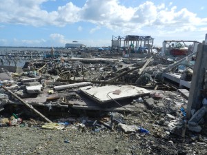 【上】パロ地区の漁港。水上の木造家屋は全壊し、遠くに避難所のコンベンションセンターが見える。