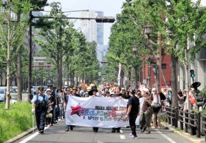 「仲良くしようぜパレード2014」と書かれた横断幕を持ち、大阪市内を行進するパレード隊。スタート地点では、隊列の最後尾が見えないほど、多くの参加者が歩道を埋め尽くしていた。（撮影／松岡瑛理）