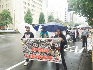 大雨の中、横断幕やプラカードを掲げてデモ行進する参加者。（東京・霞が関。撮影／片岡伸行）